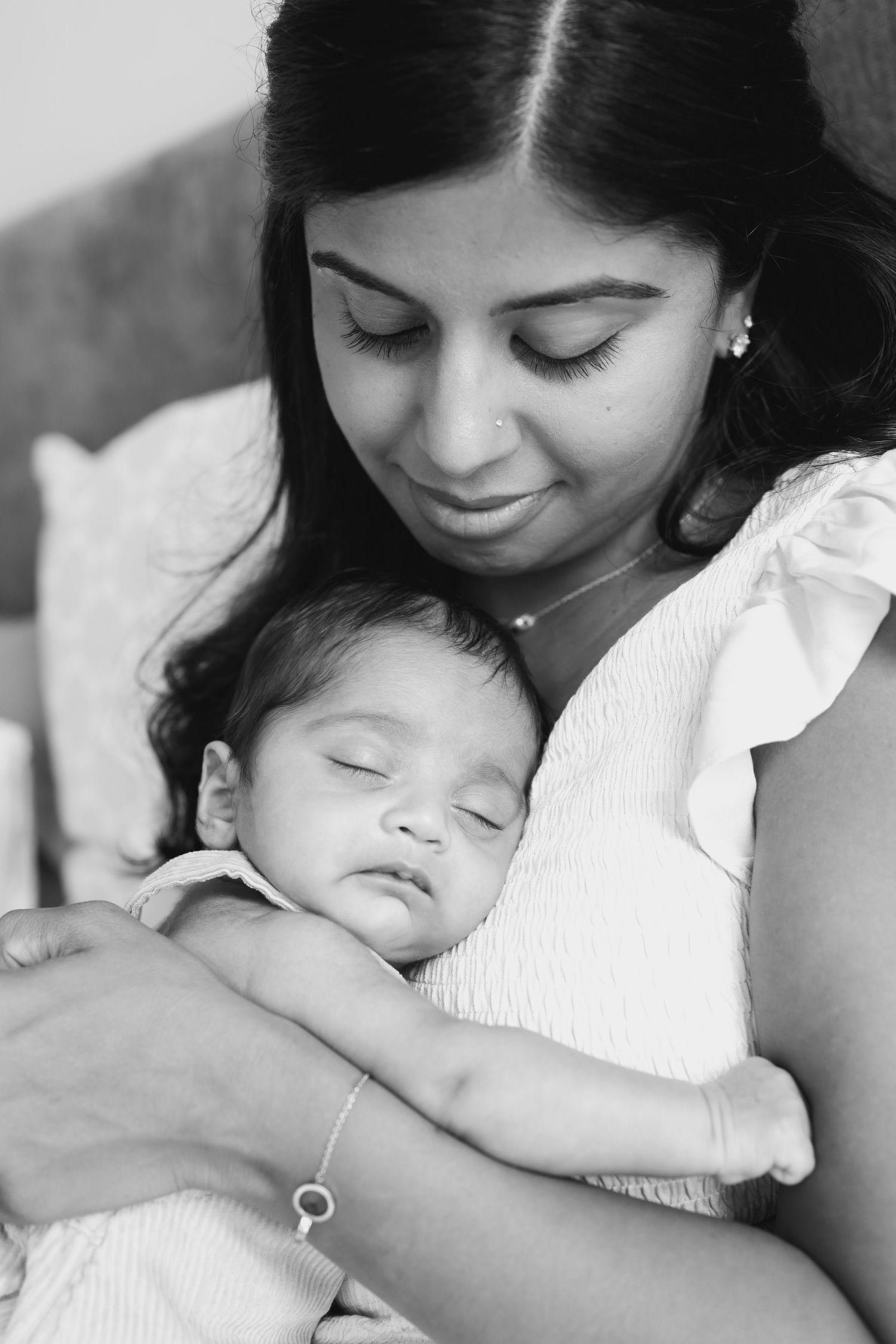 A tender black and white portrait of a mother holding her sleeping baby against her chest.