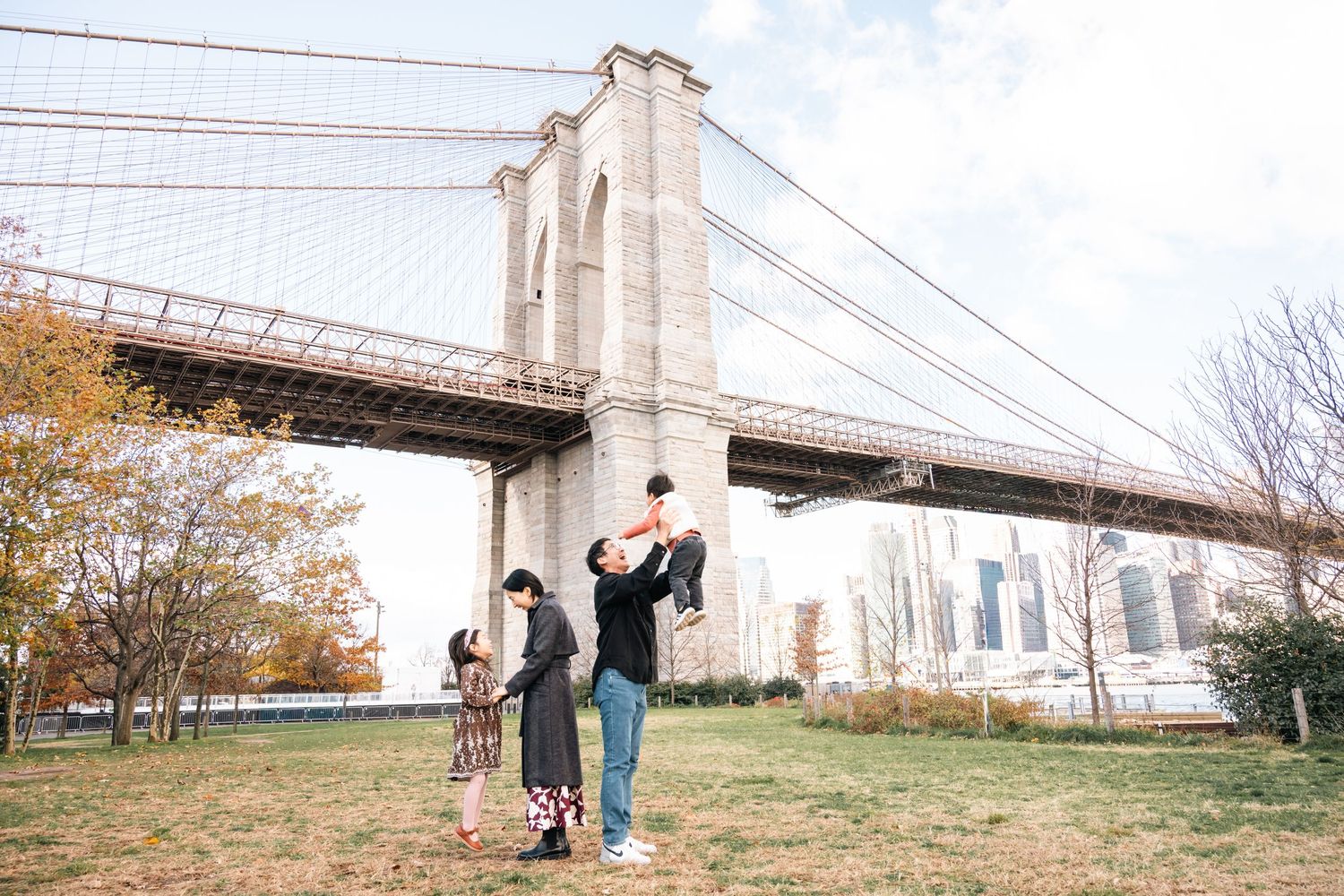 People enjoying a scenic autumn day near the Brooklyn Bridge with fall foliage and city views in the background.
