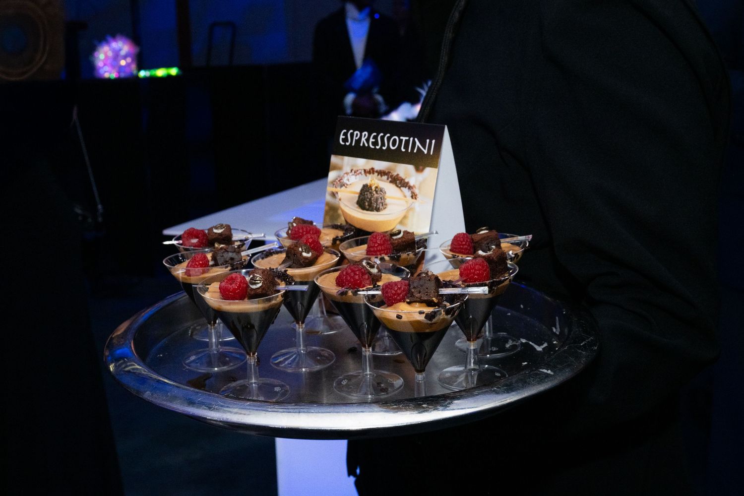 A server holds a tray of chocolate espressotini desserts at a catered event.