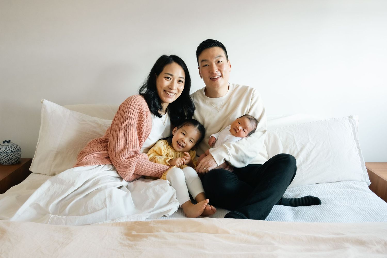 Family relaxing together on white bedding during lifestyle photo session.
