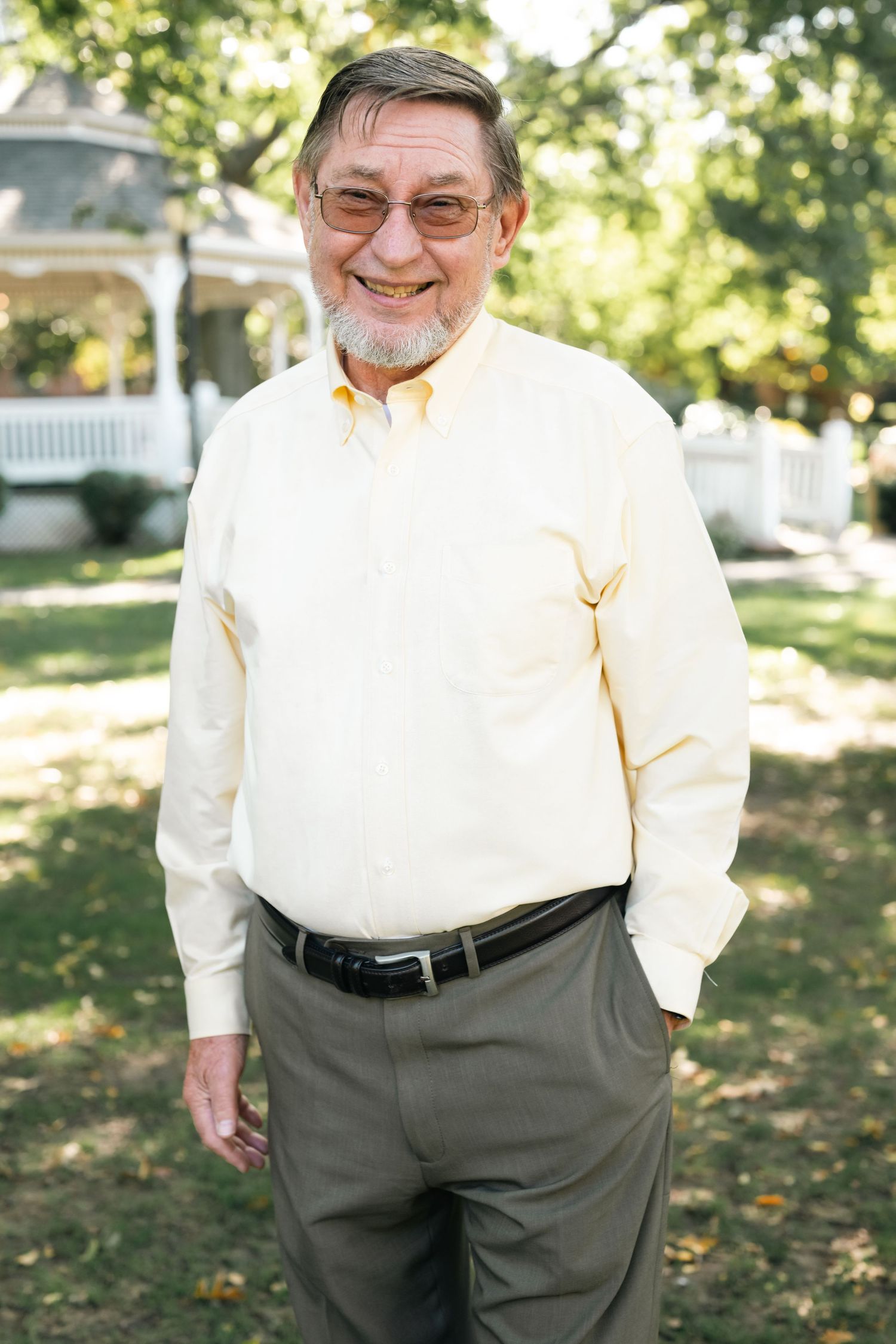 Person in white shirt and gray slacks standing outdoors with a warm smile.