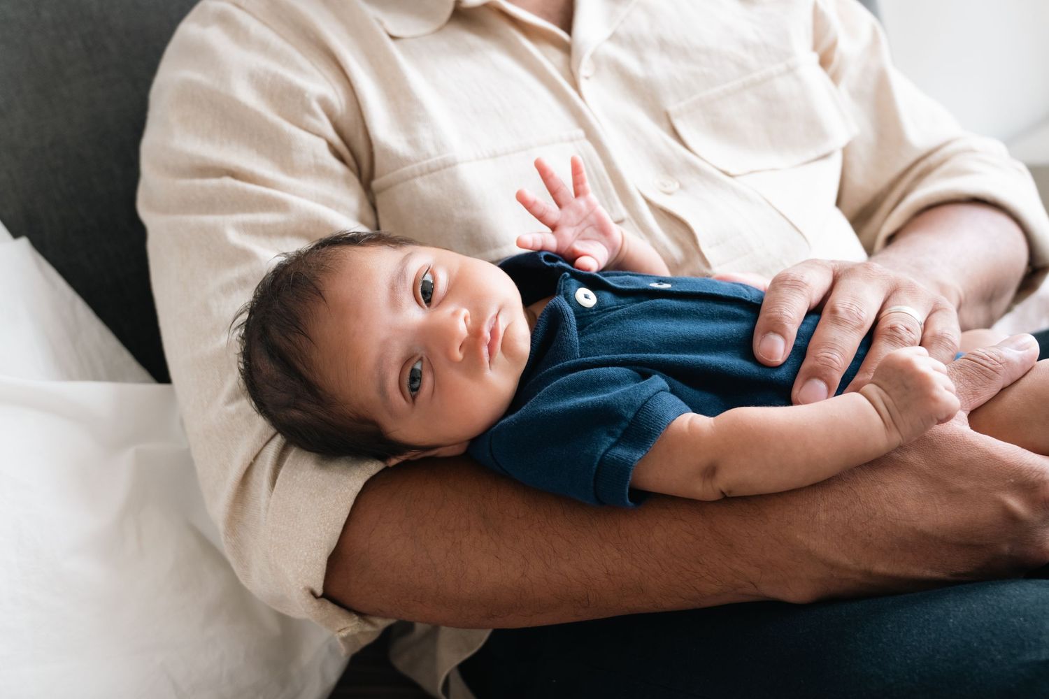 Parent in white shirt holding sleeping newborn baby on grey couch.