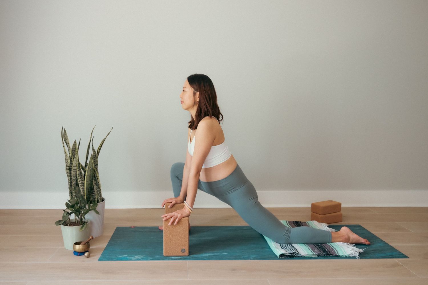 Series of yoga stretches being performed on a teal mat with wooden blocks and houseplants.