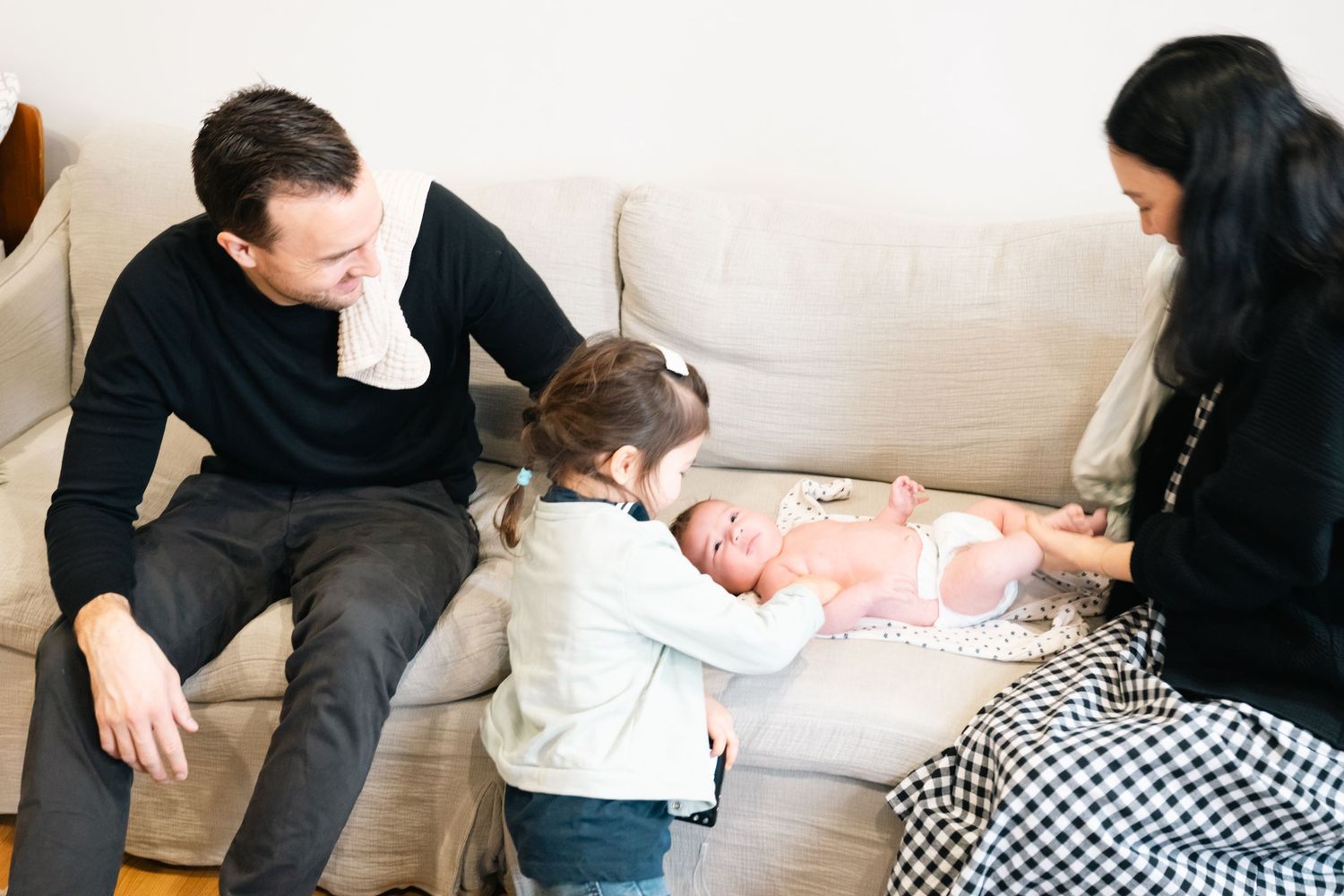 A tender family moment shared on a cream-colored couch with a sleeping newborn baby.