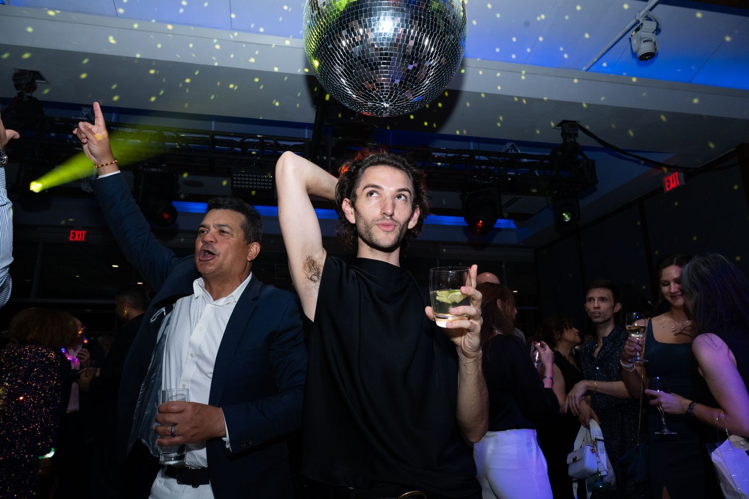 Man dancing under disco ball holding cocktail at an upscale indoor evening party celebration.