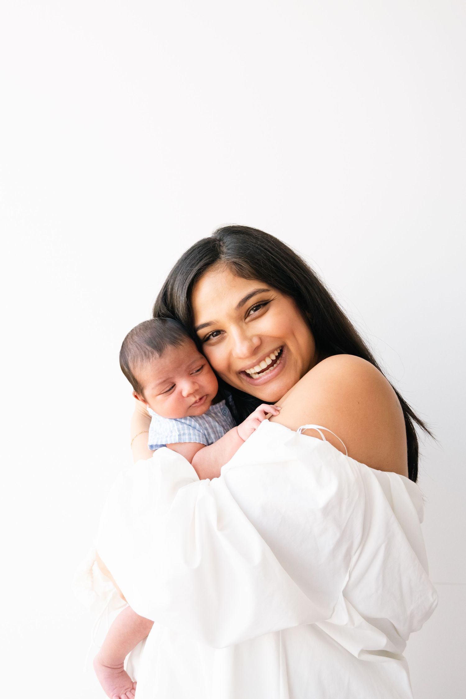 Joyful parent in white top holds sleeping newborn baby against minimalist white background.