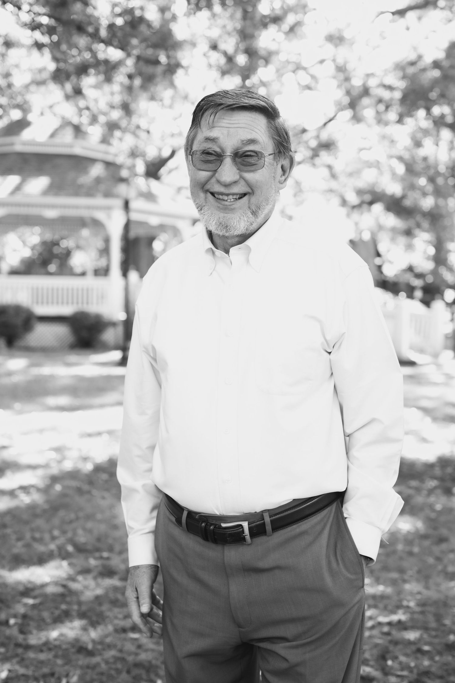 Portrait of senior man in white button-down shirt smiling outdoors in black and white.