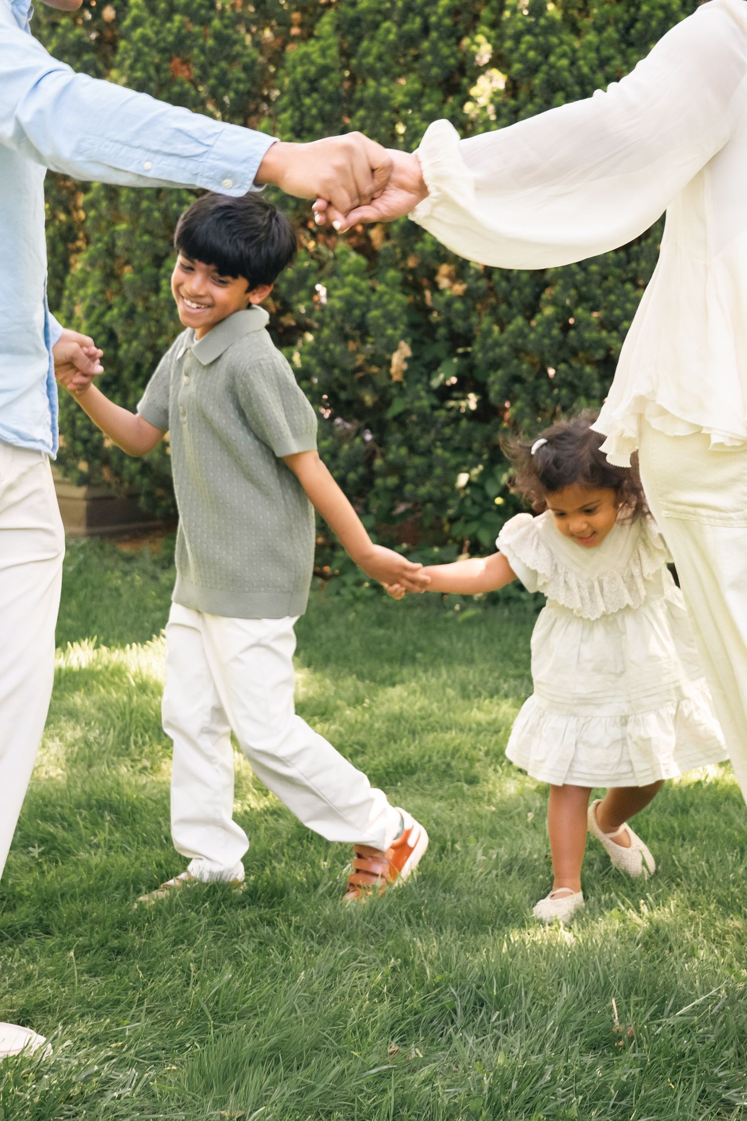 Family holding hands and playing together on green grass in a sunny backyard garden.