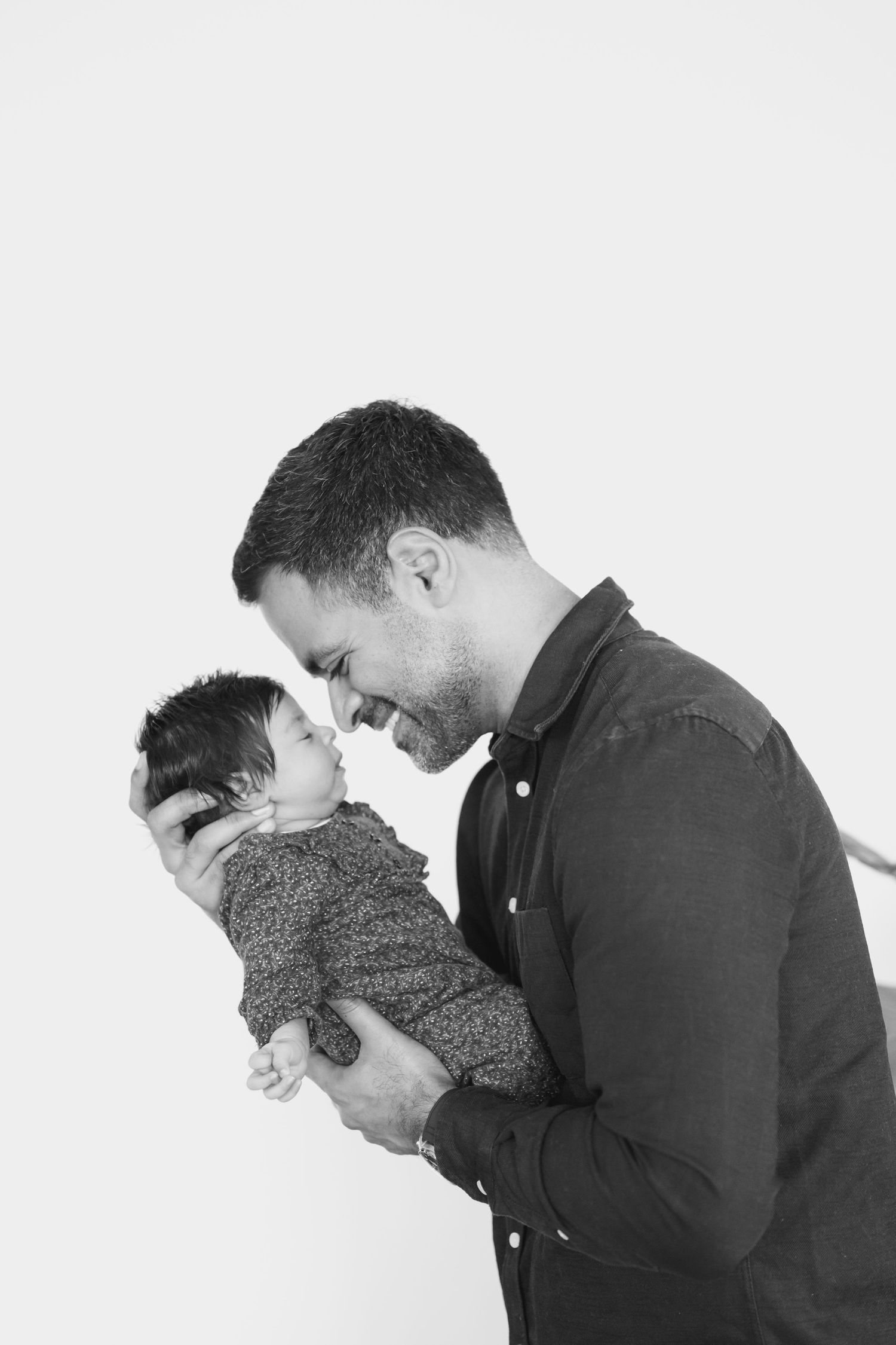 Black and white photo of a smiling man tenderly holding a newborn baby close to his face.