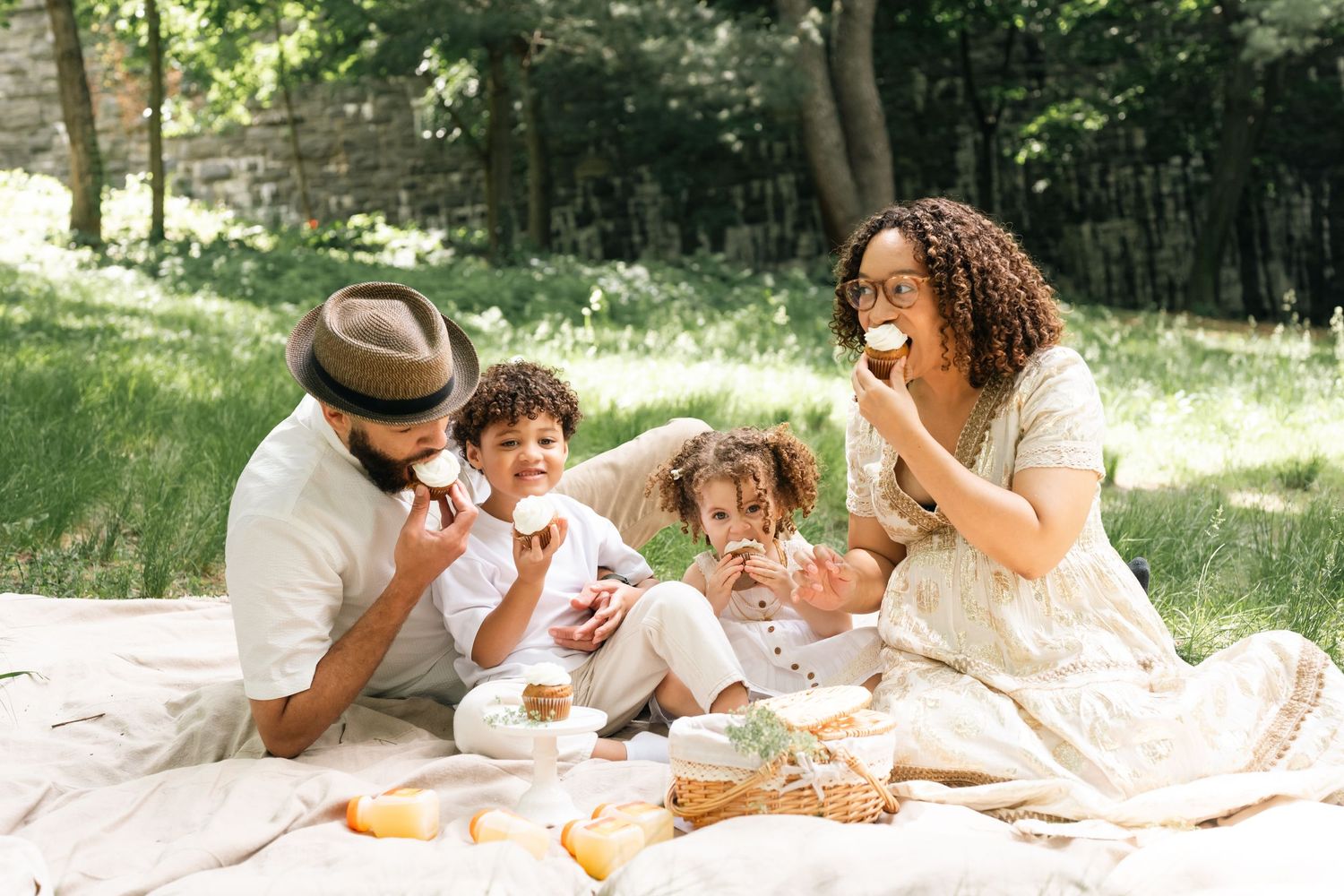 Happy family enjoying a sunny outdoor picnic on a blanket, eating fruit together in a lush green park.