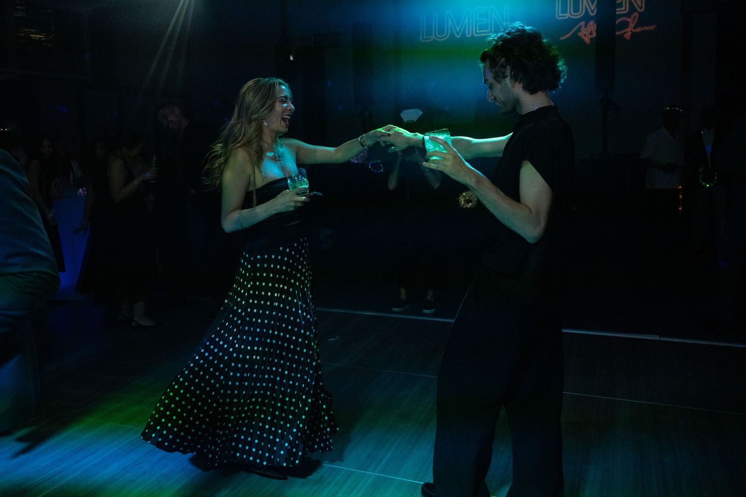 A couple dances together under green and blue lights on a crowded gala dance floor.