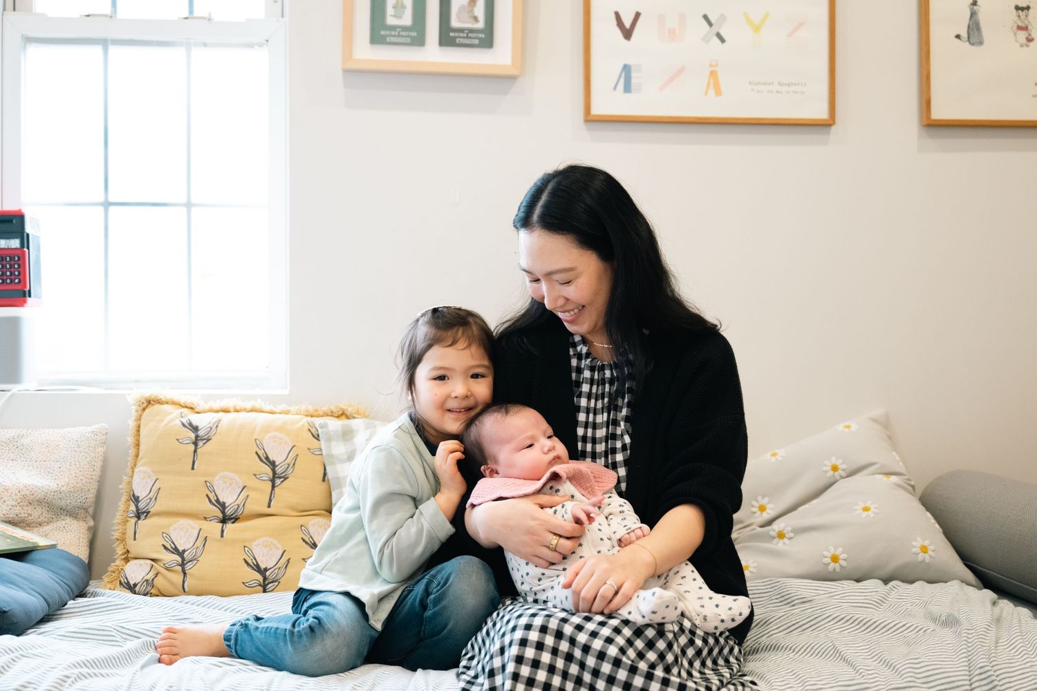 A cozy family moment on a bed with yellow deer-print pillows as they cuddle together in a sunlit room.