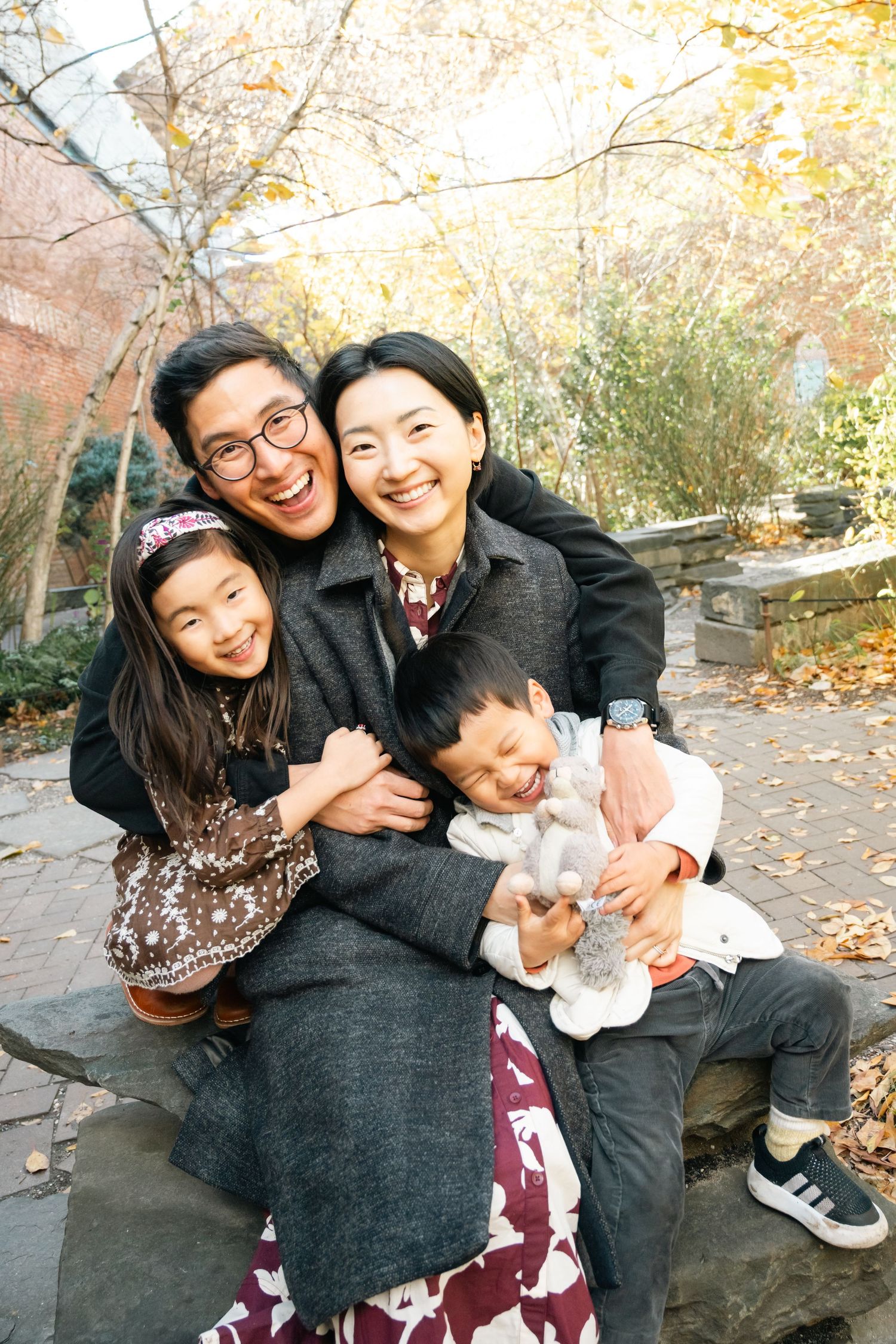 A playful family moment captured in autumn with fallen leaves and natural lighting in the background.