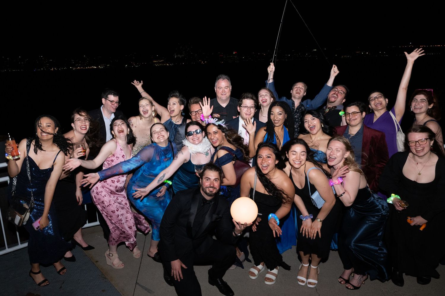 Large group of elegantly dressed people posing together at an outdoor nighttime formal event.