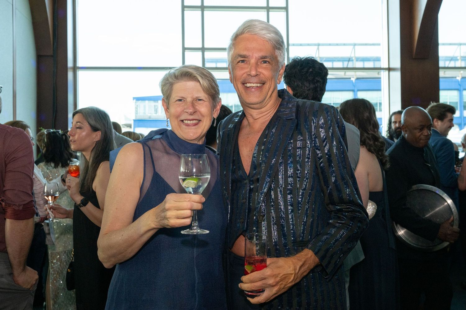 Smiling couple holds wine glasses and poses together at a festive evening cocktail party.