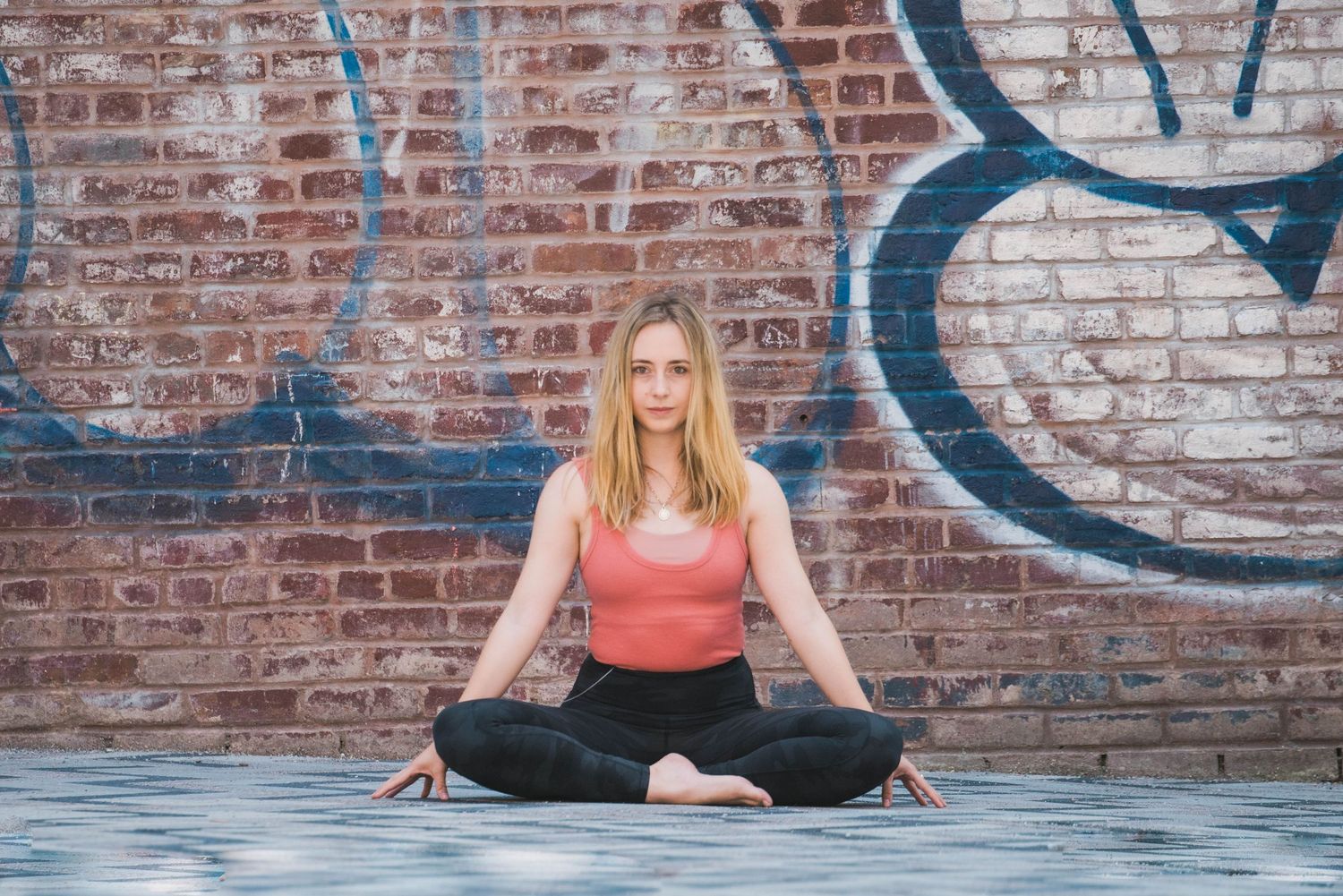 Person in coral top doing yoga poses against rustic brick wall with graffiti.