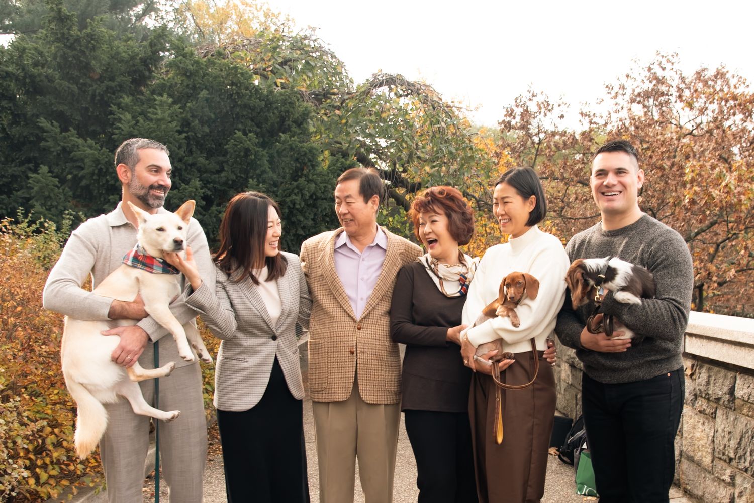 Group photo of family members holding small dogs on a stone bridge during autumn.