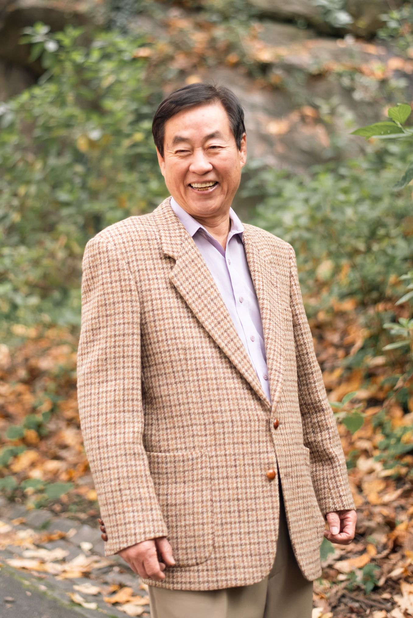 A person wearing a tan plaid blazer smiles warmly during an autumn photoshoot.