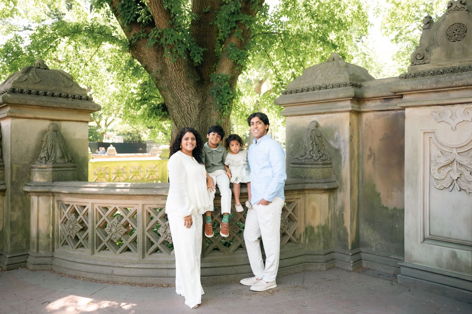Family of three posing together at Bethesda Terrace in Central Park, surrounded by lush greenery.