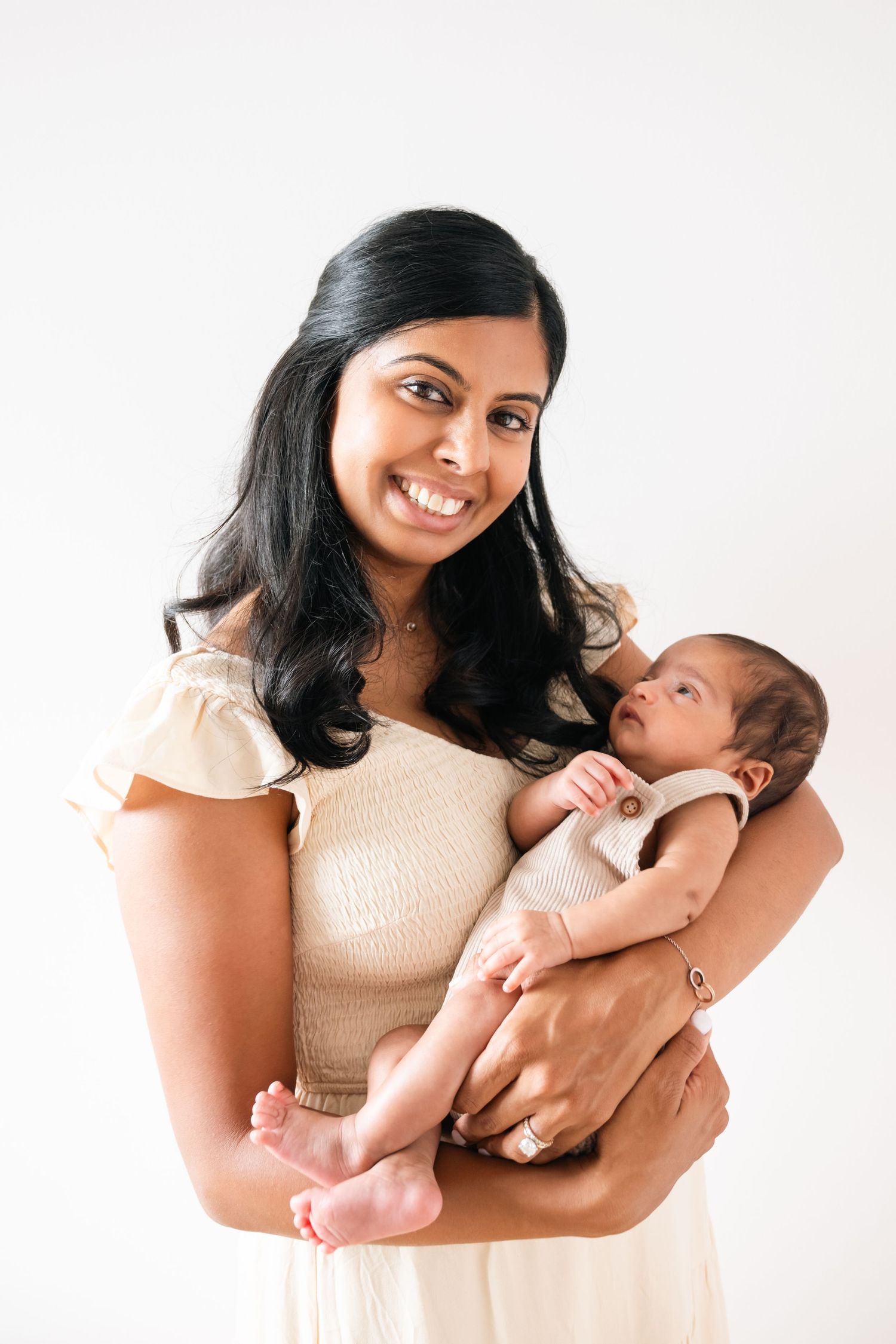 Mother in cream dress holds and gazes lovingly at newborn baby during photo session.
