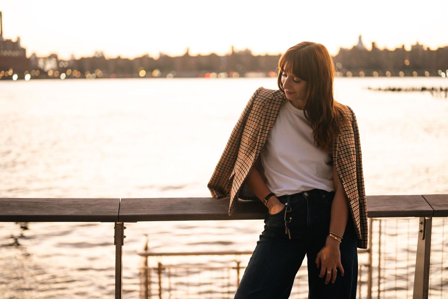 Sunset waterfront portrait series with figure sitting on railing against golden sky.