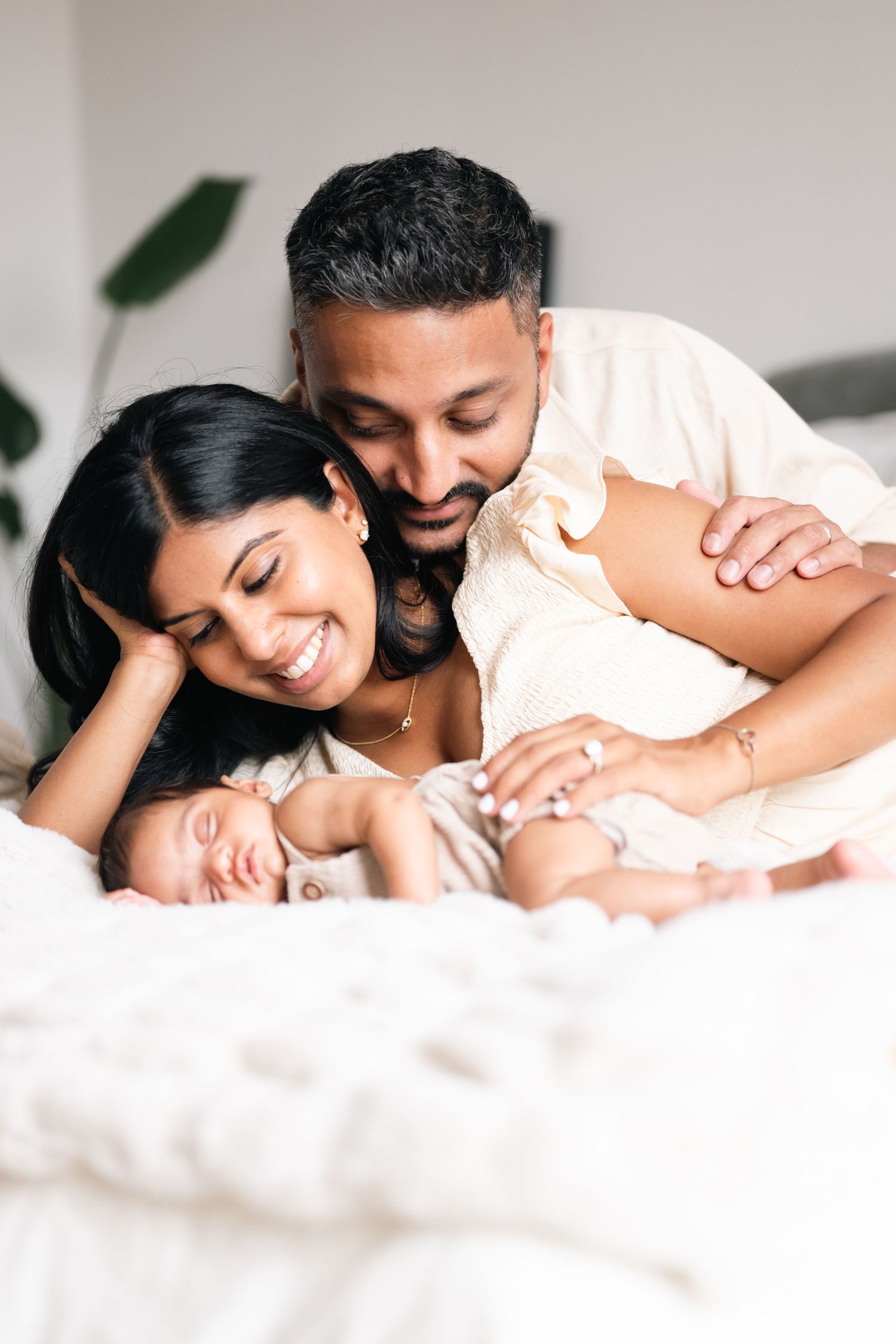 Intimate family moment with parents cuddling their newborn baby on white bedding.