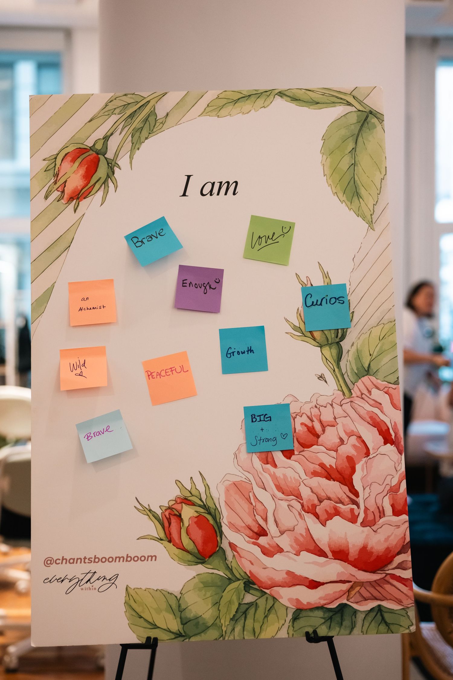 Floral display board with colorful sticky notes reading empowering affirmations under 'I am' heading at a wellness event.