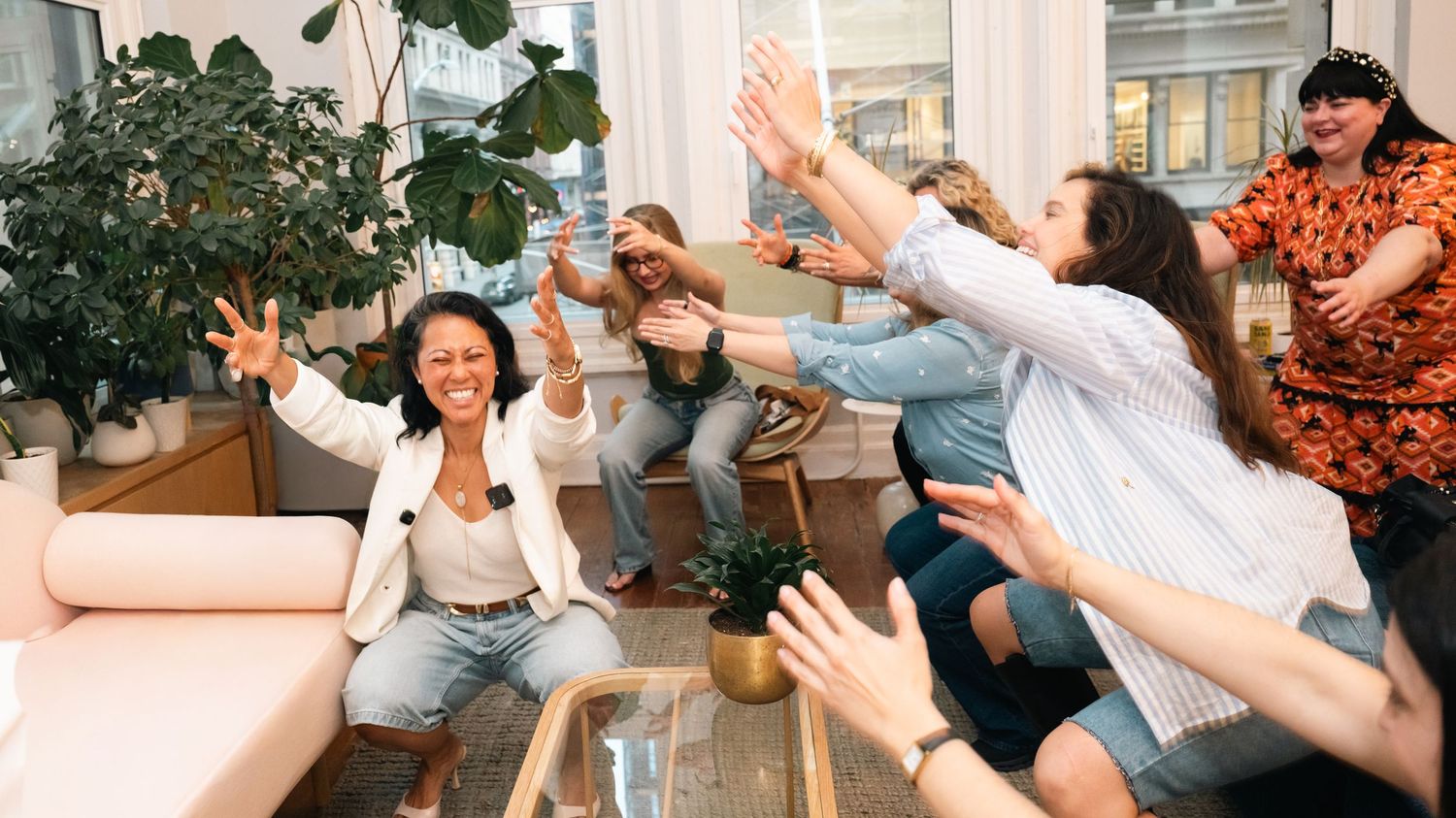 Group of diverse women celebrating together in a modern office lounge, giving high fives and peace signs.
