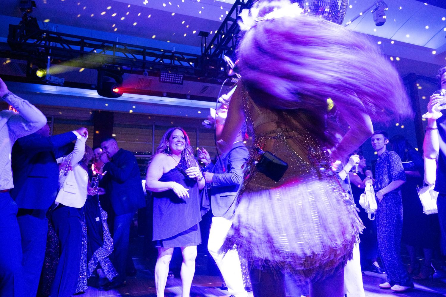 Energetic crowd dancing at a vibrant nightclub event with purple lighting and confetti falling.