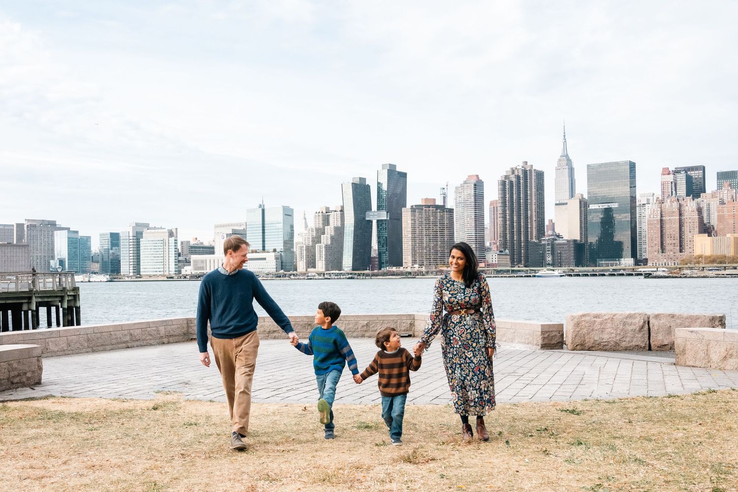 Family walking along waterfront path with Manhattan skyline visible in the distance.