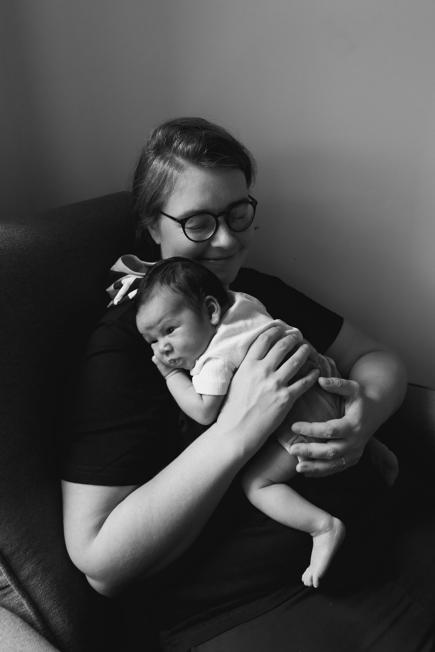 Black and white portrait of person holding infant on couch.
