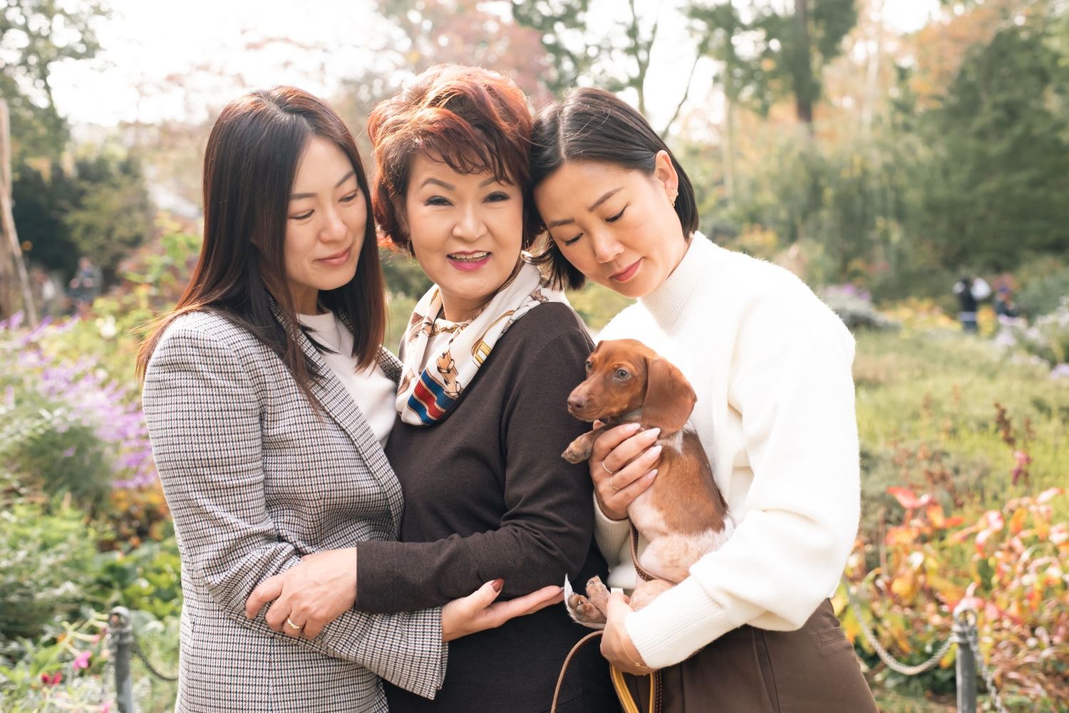 Three people share warm hugs and smiles during a fall photoshoot in a garden setting.