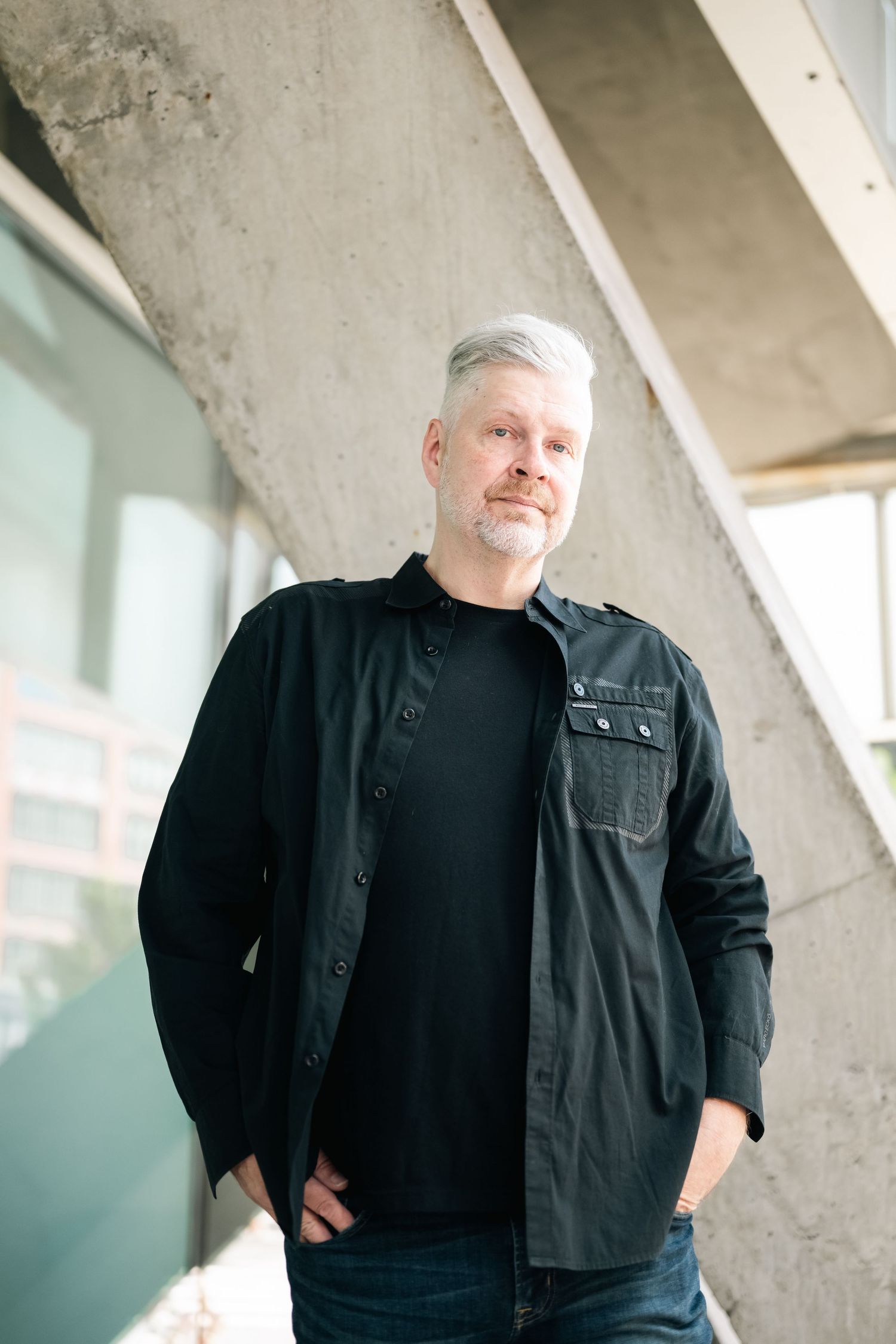 Person in black attire posing against concrete architectural elements.