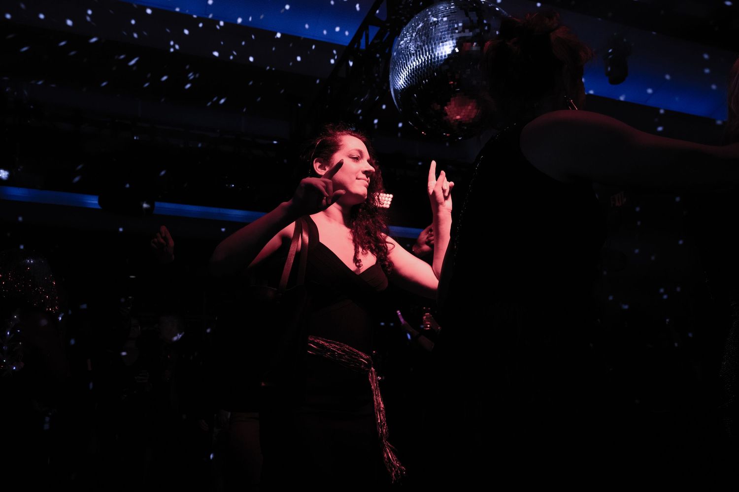 Female singer performs passionately in black dress under a glittering disco ball at a glamorous evening event.