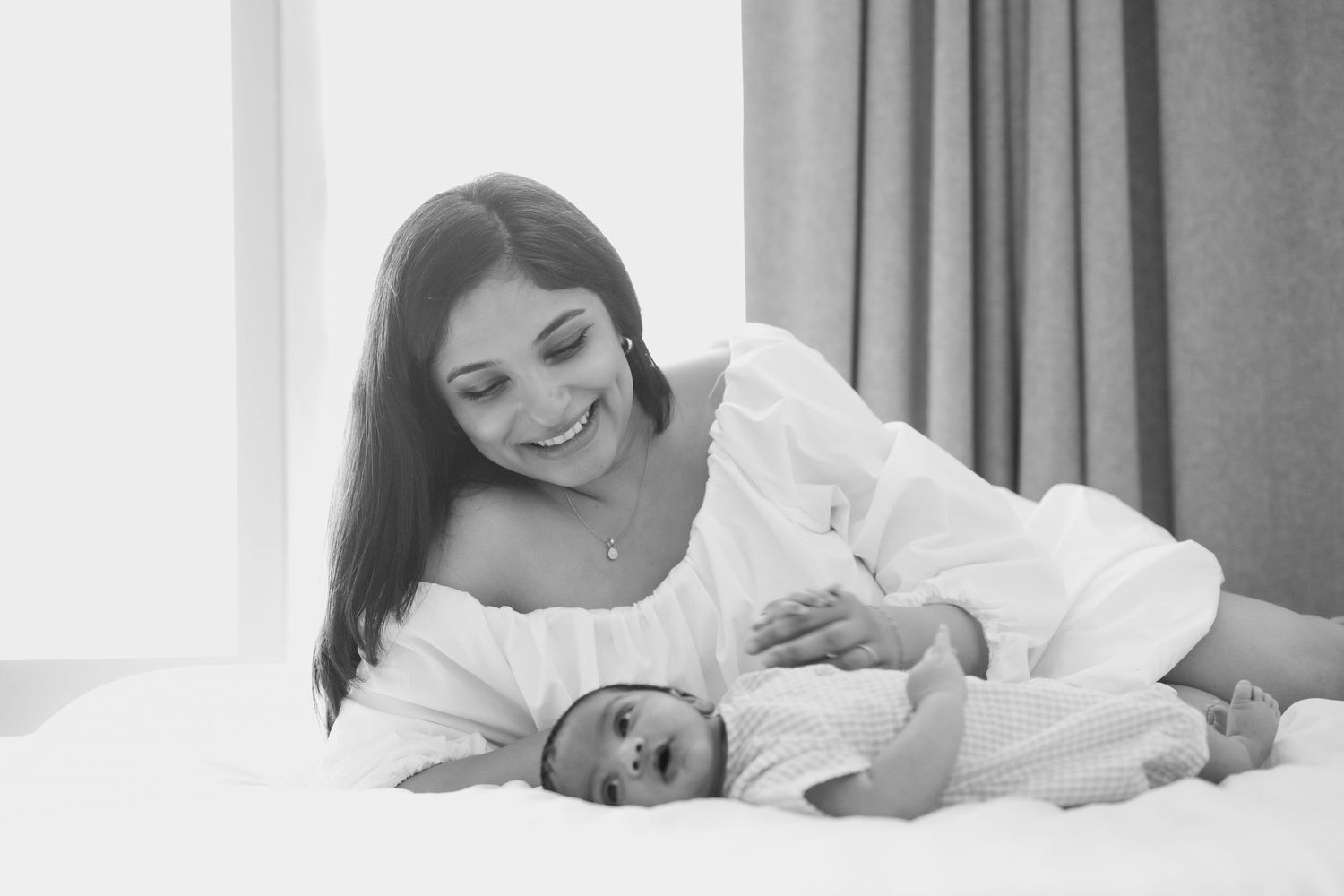 Mother and baby sharing tender moment while lying on white bedding.