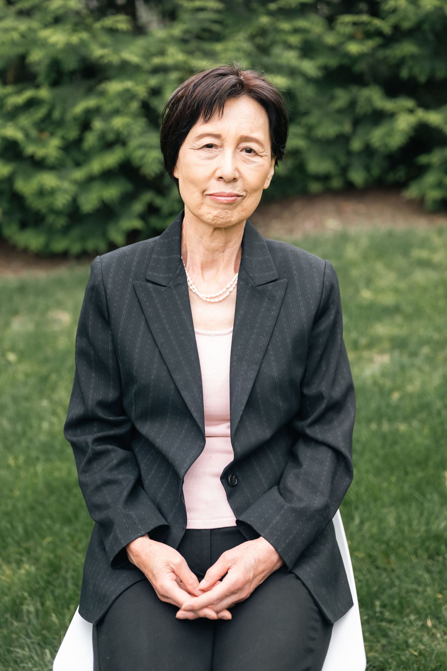 A person in formal business attire sits thoughtfully on a white chair outdoors.