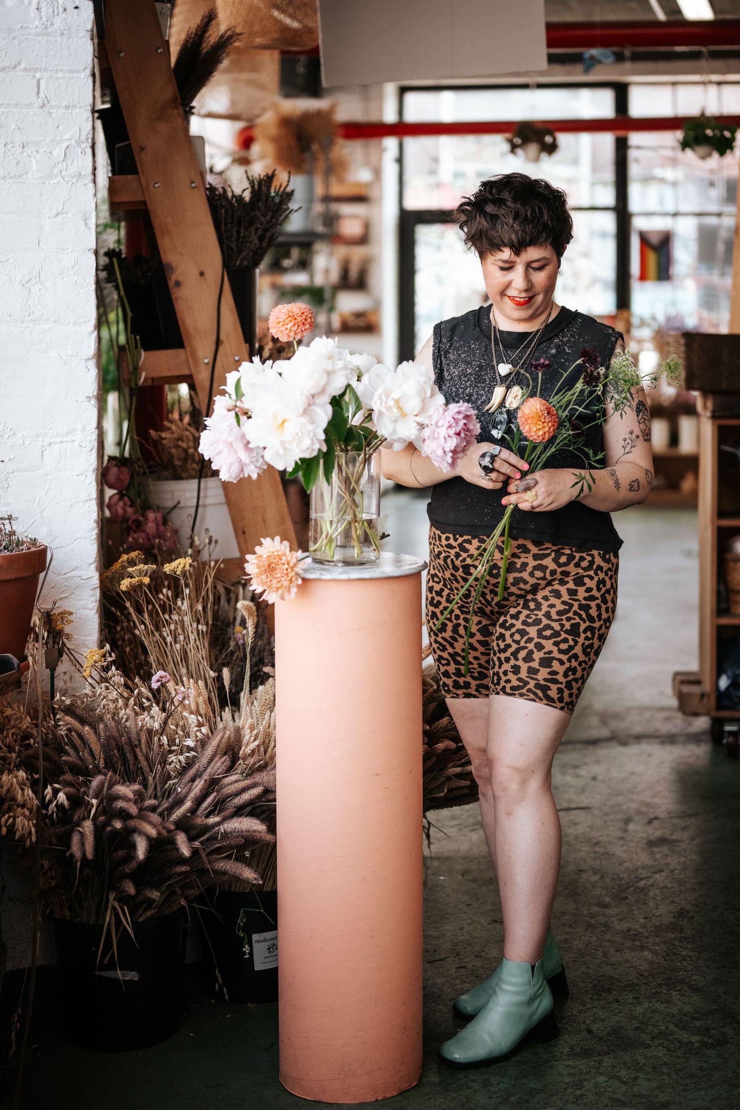 Person in leopard print and boots arranging flowers in a peach-colored vase.