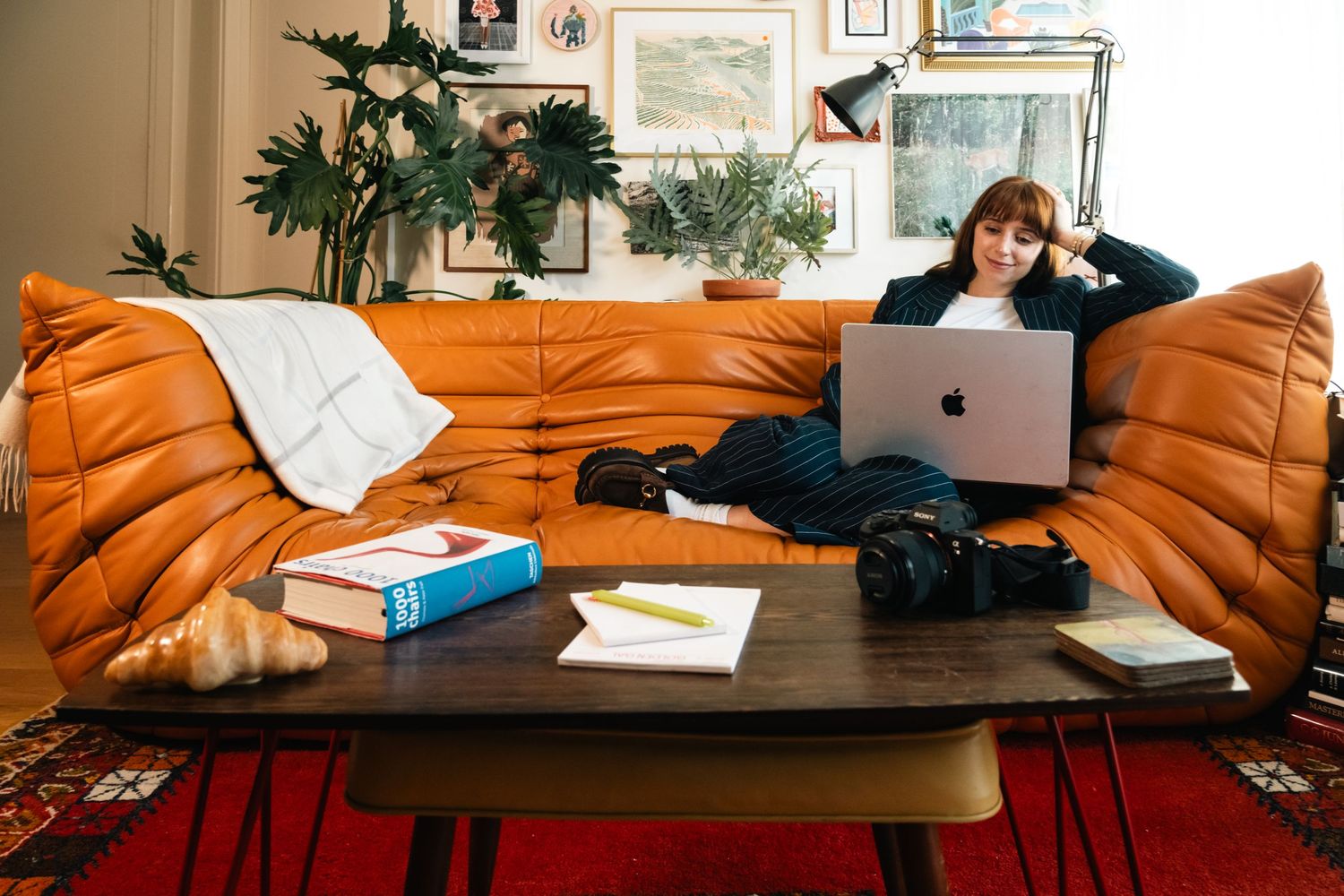 Person relaxing on an orange couch while working on a laptop in a cozy home office setting.