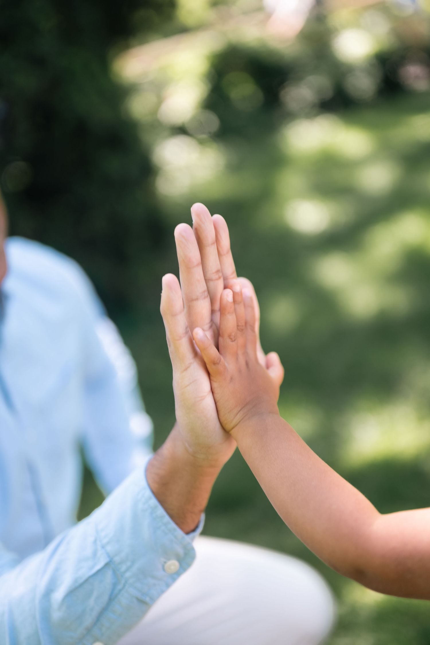 Adult and child pressing palms together outdoors in a green park setting, symbolizing connection and togetherness.