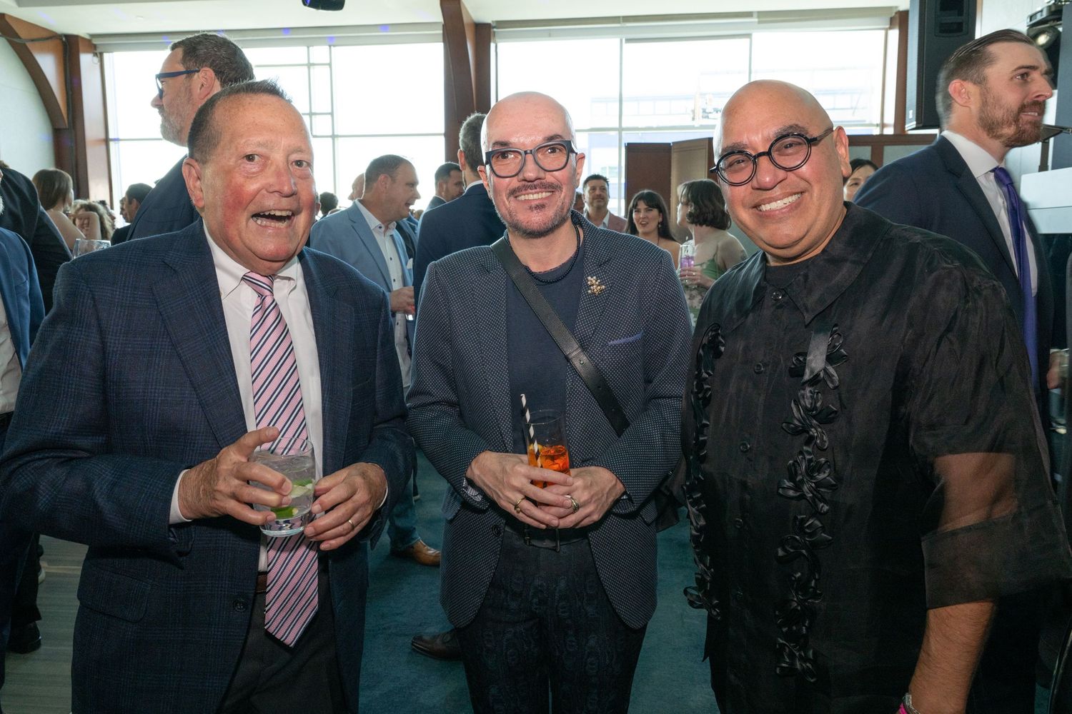 Three men smiling and holding drinks at a sophisticated networking event.
