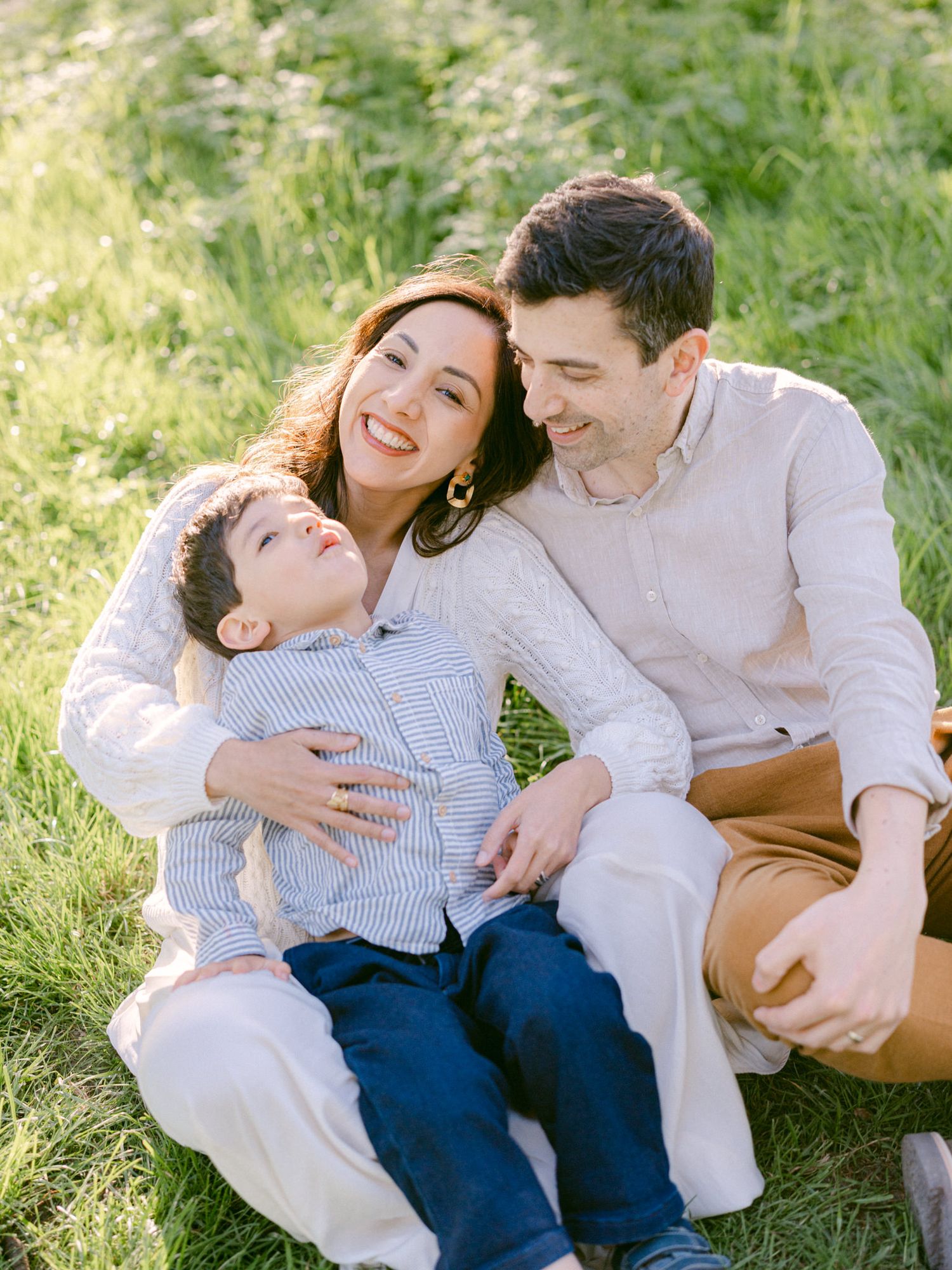 A couple reclines together on lush green grass during an intimate outdoor photoshoot on a sunny day.
