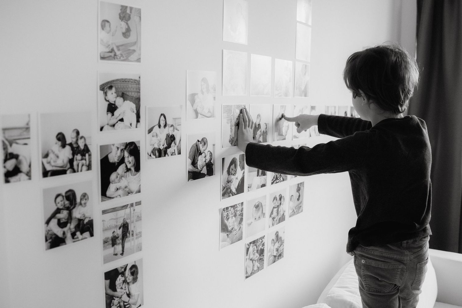 Silhouette accrochant des photographies sur un mur blanc, en noir et blanc.