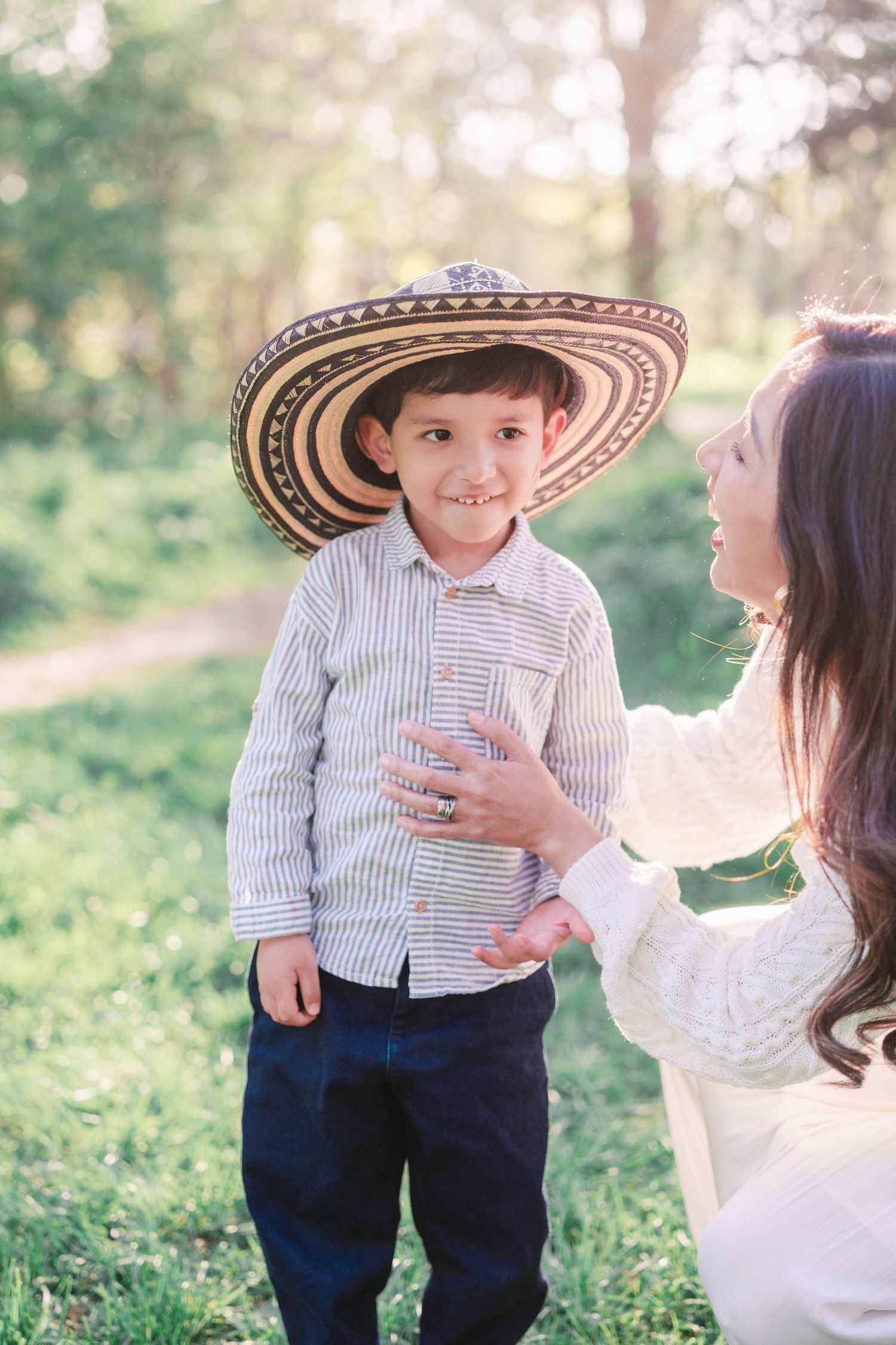 A child wearing a traditional Colombian sombrero vueltiao and striped shirt stands outdoors with an adult in a natural setting.