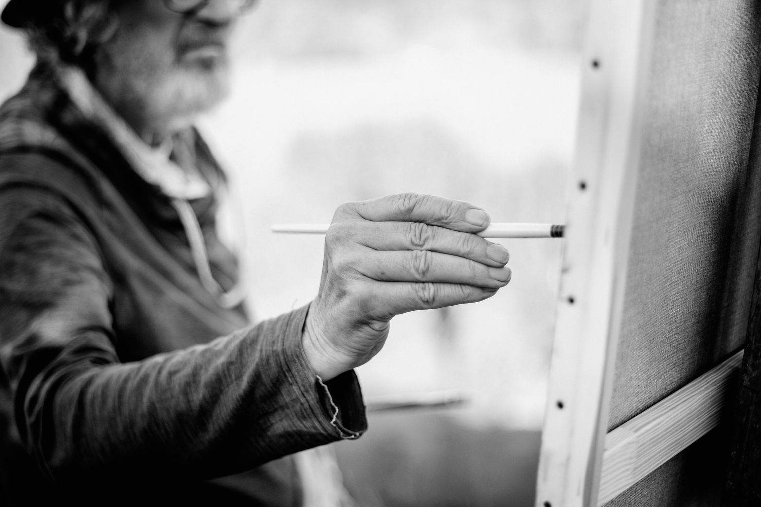 Black and white photo of an artist painting on canvas with a brush, captured in close-up detail.