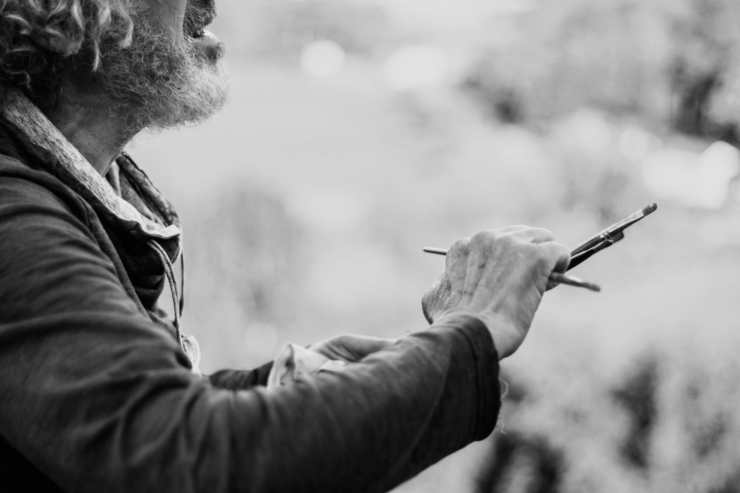 Black and white photo of a man holding a paintbrush outdoors, captured in profile view.