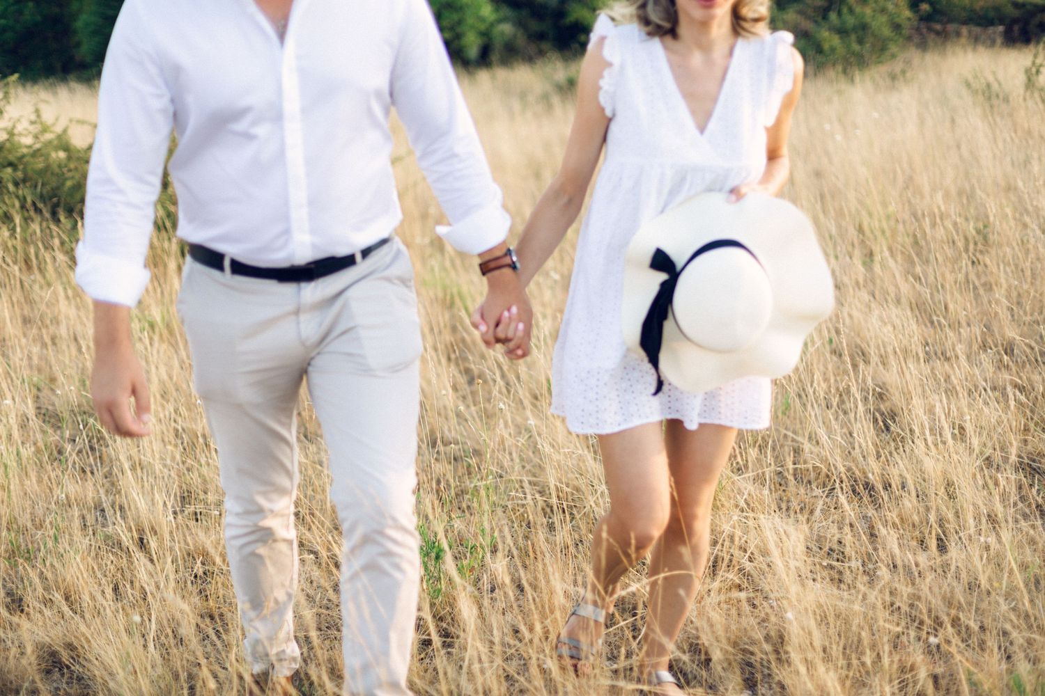 Two people wearing white outfits walk together through a sun-dried field of tall grass on a bright autumn day.