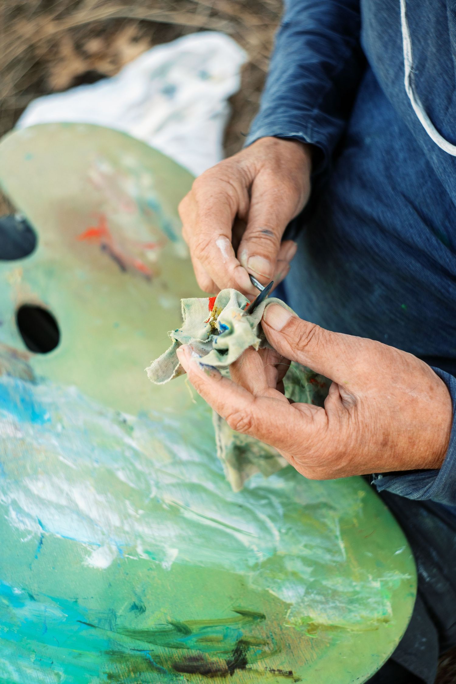 Artist squeezing paint from tubes onto a colorful palette, with paint-stained hands close-up.