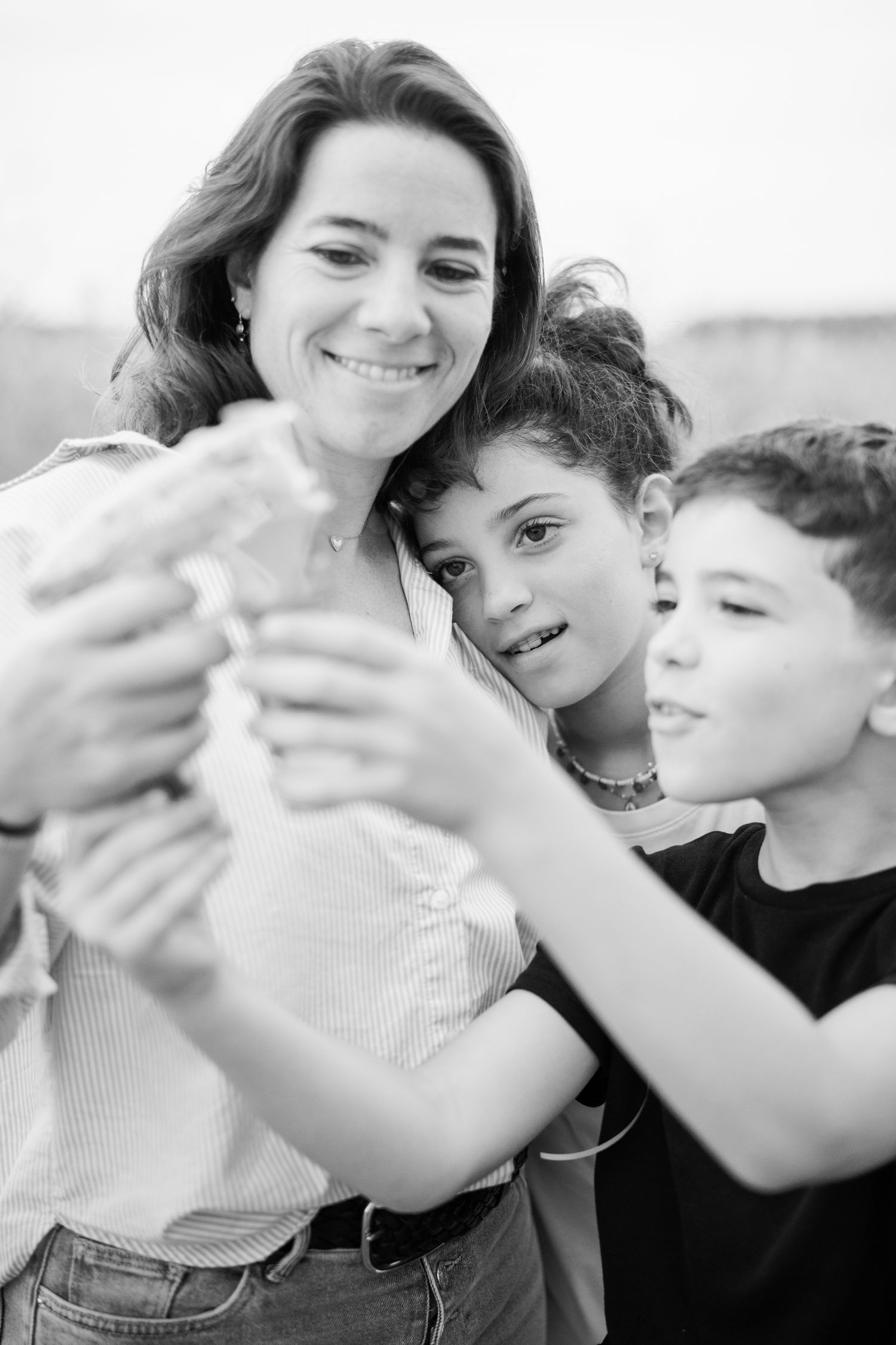 Black and white photo of a smiling mother with two children examining something together outdoors.