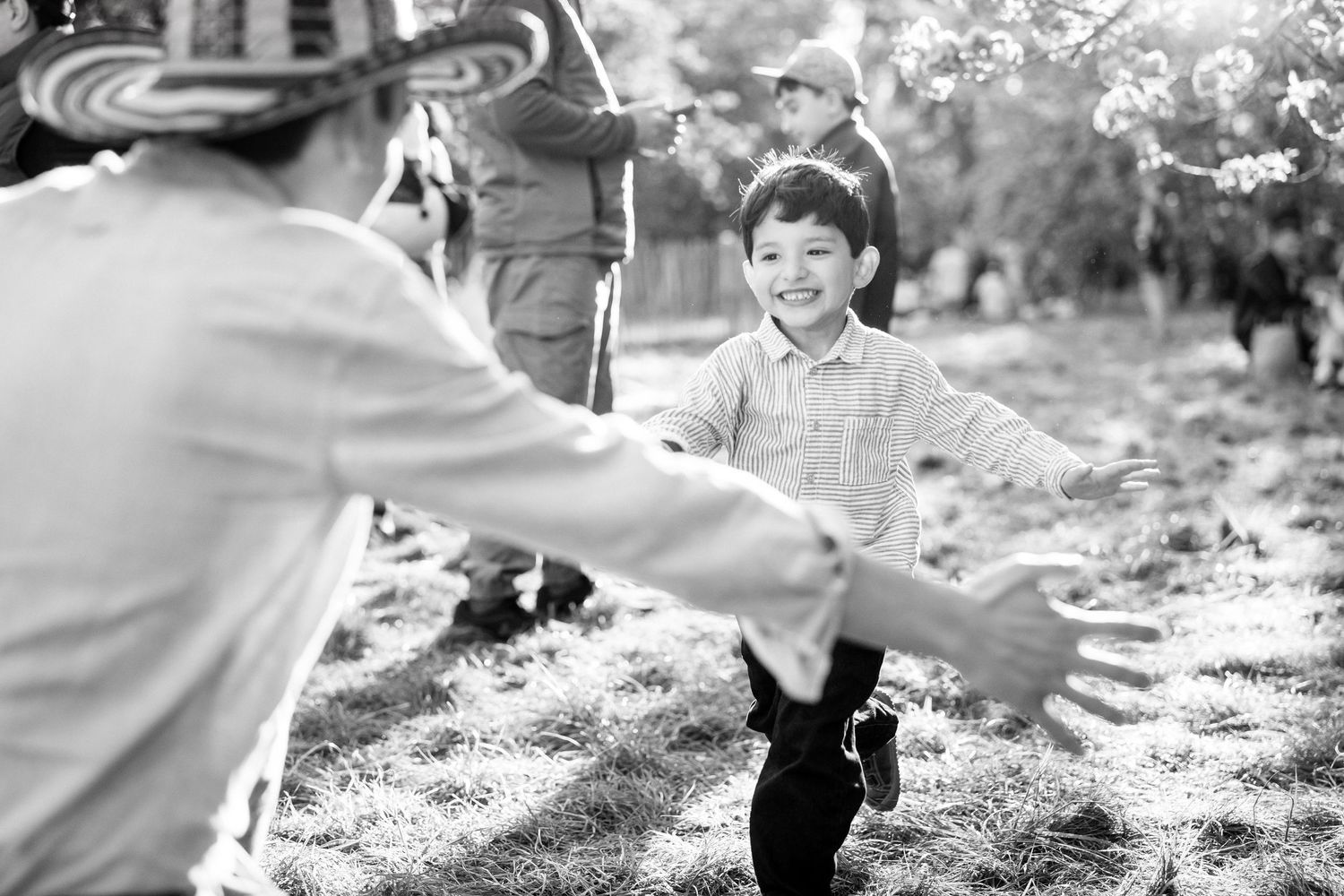 Black and white photo of a smiling boy running with open arms toward an adult outdoors.