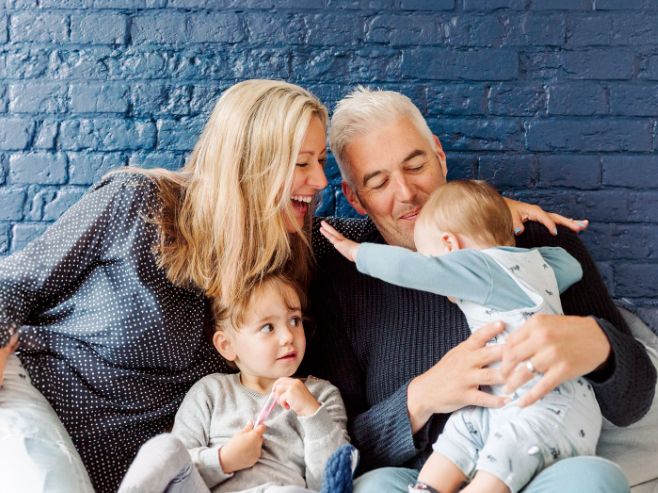 Happy family with two toddlers sharing a joyful moment against a blue brick wall background.